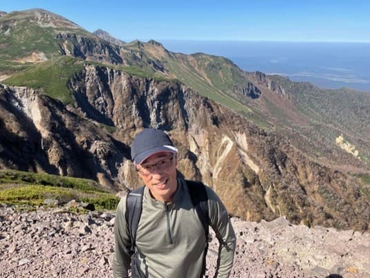 山崎正臣氏が山の前で微笑む様子